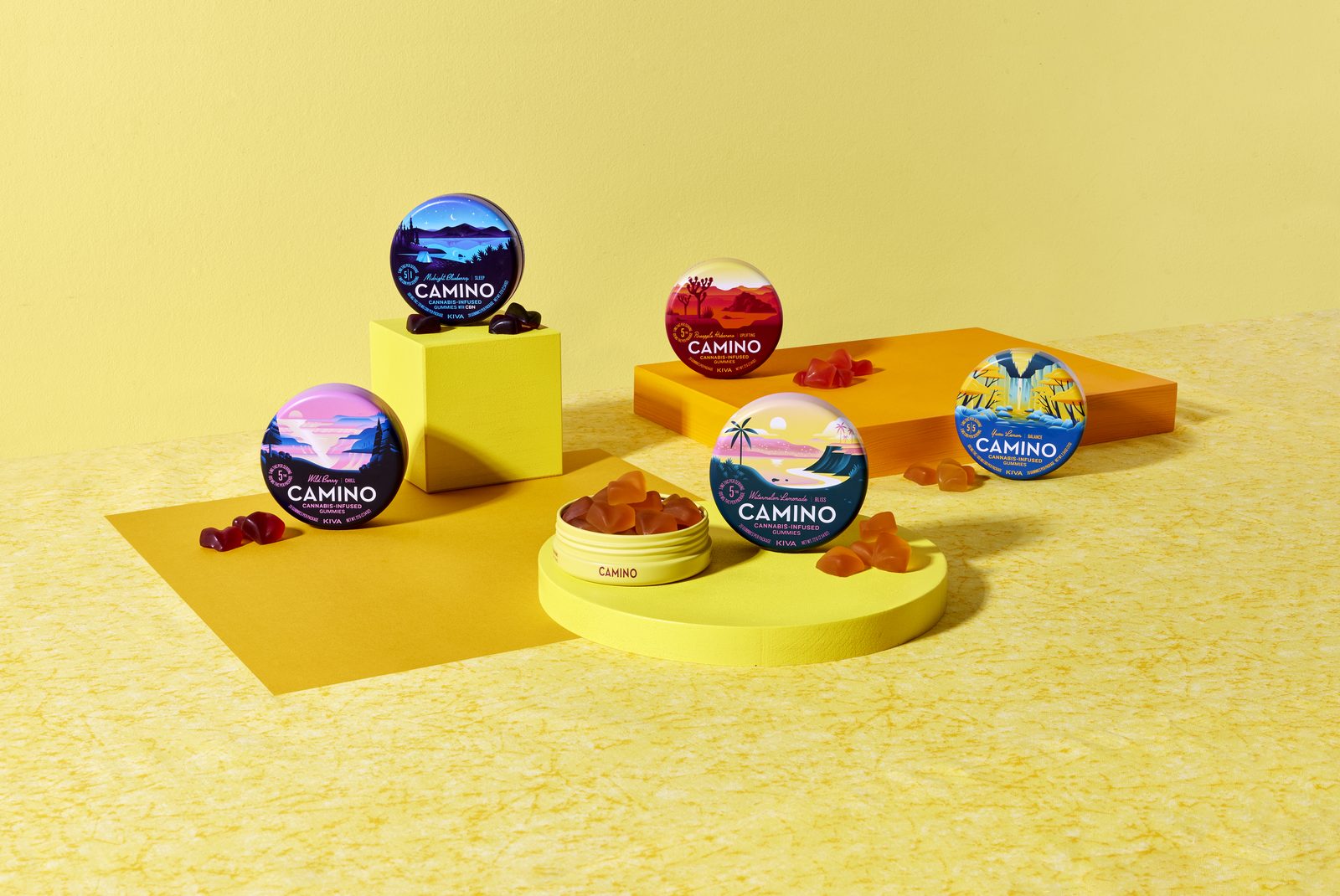 Camino gummy tins arranged on yellow geometric pedestals with gummies scattered around